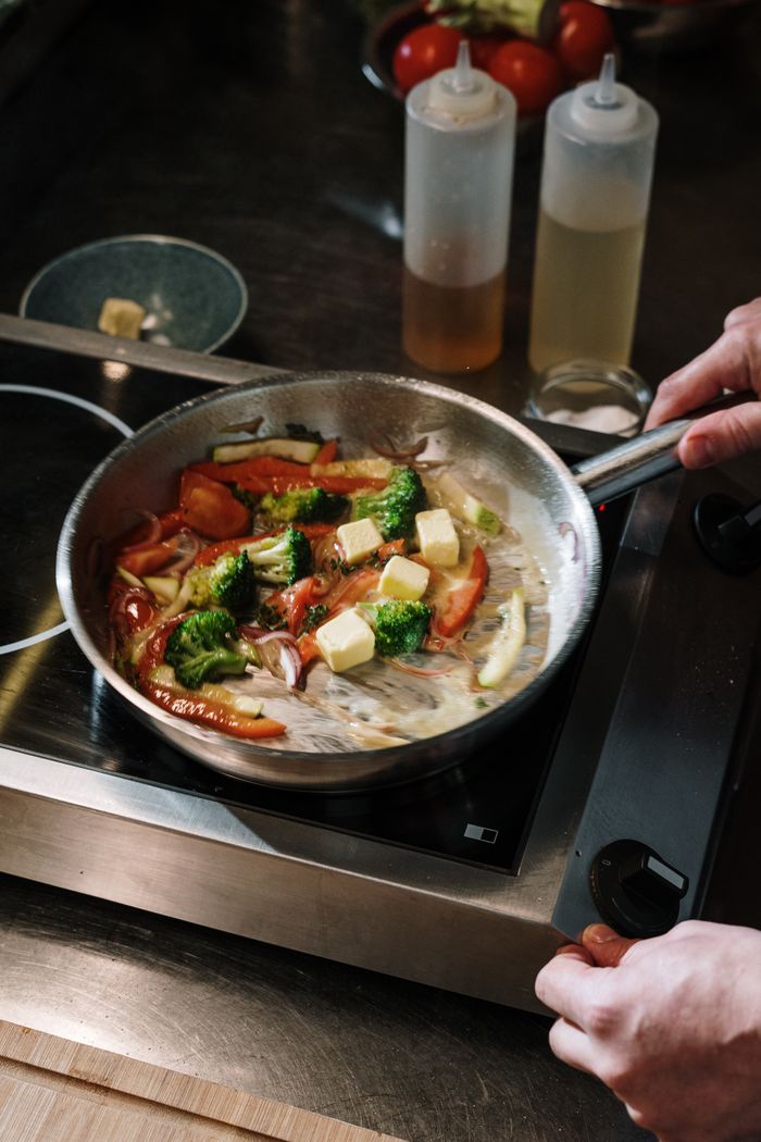 A chef cooks colorful vegetables in a skillet with butter on a stove in the kitchen.